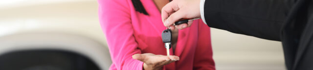 A man in a suit hands over car keys to a woman in a pink blouse, symbolizing a transaction or agreement.