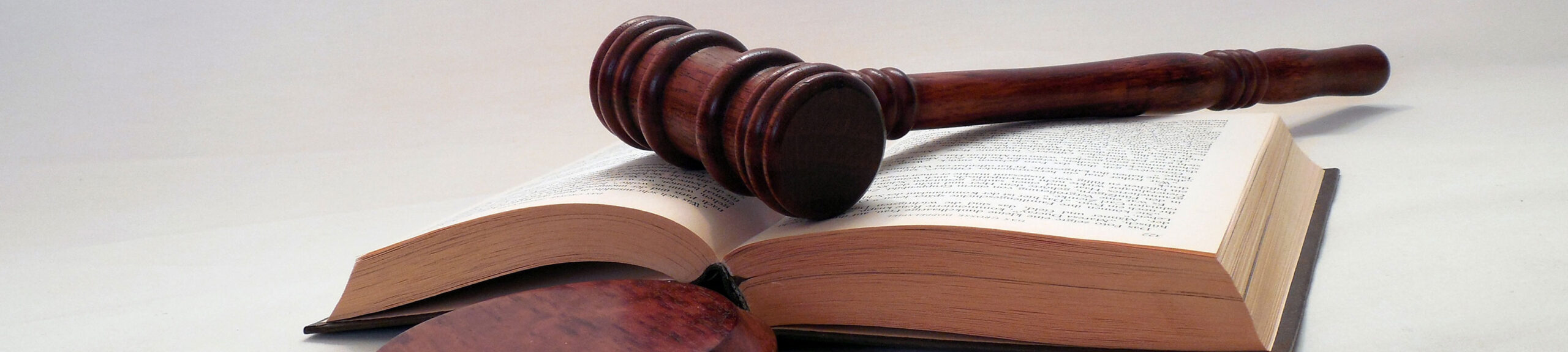 A wooden gavel rests on an open law book, symbolizing legal authority and the judiciary, against a neutral background.