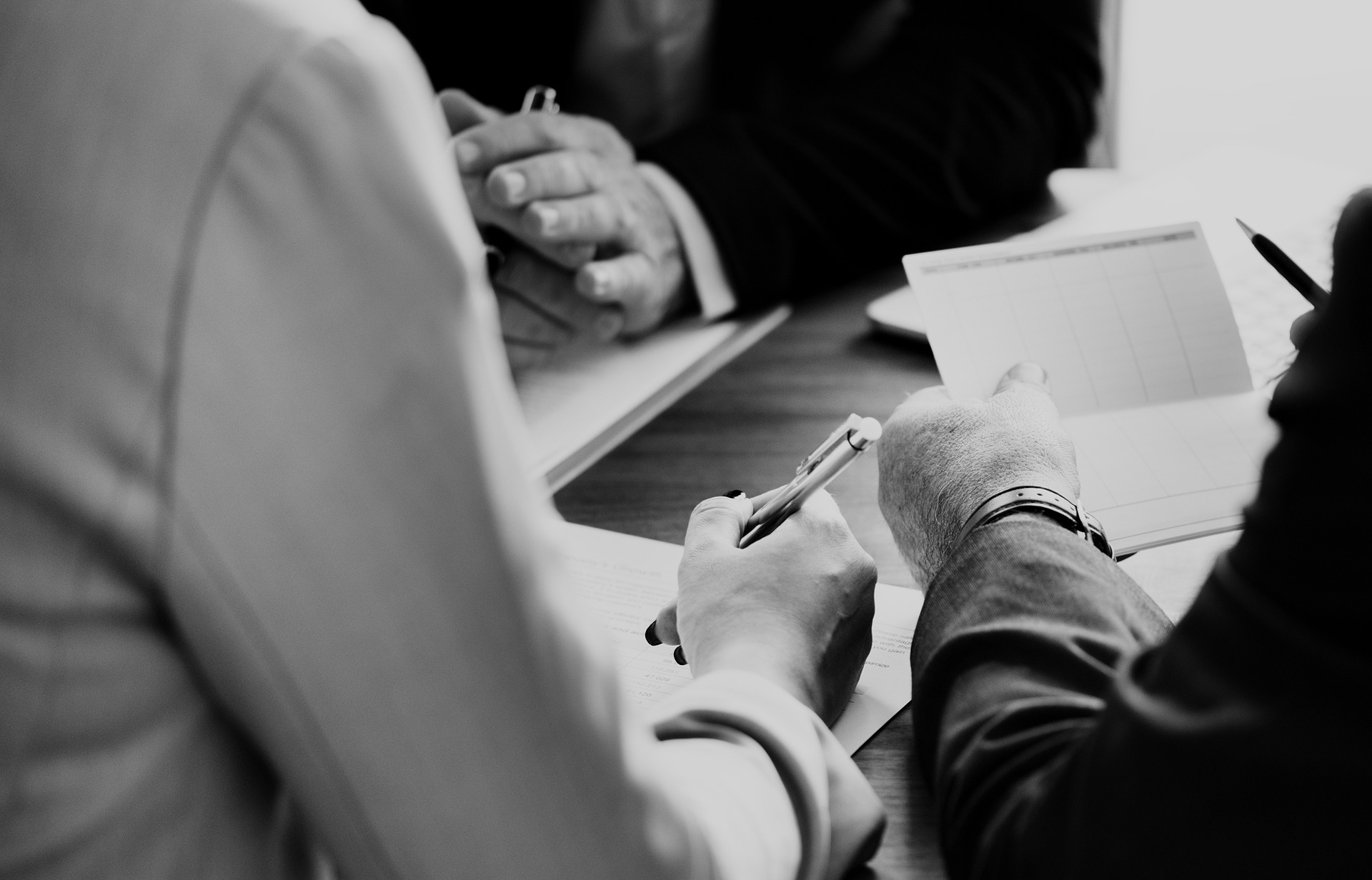 Black and white image of a divorce mediation meeting with three people discussing documents, one person taking notes, and another pointing at a paper.