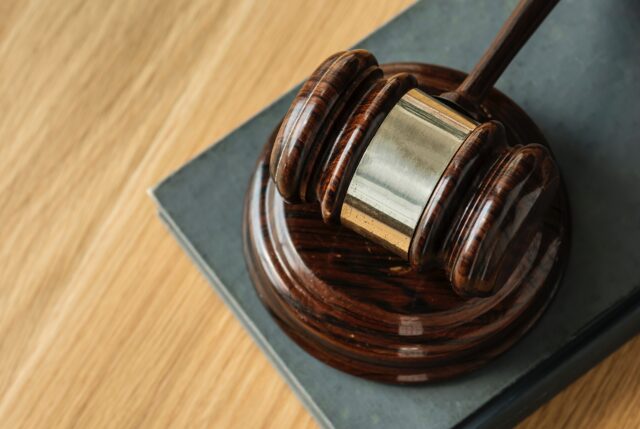 A wooden judge's gavel rests on its sound block, situated on a book about domestic violence in New Jersey, with a brown cover, all placed on a wooden tabletop.