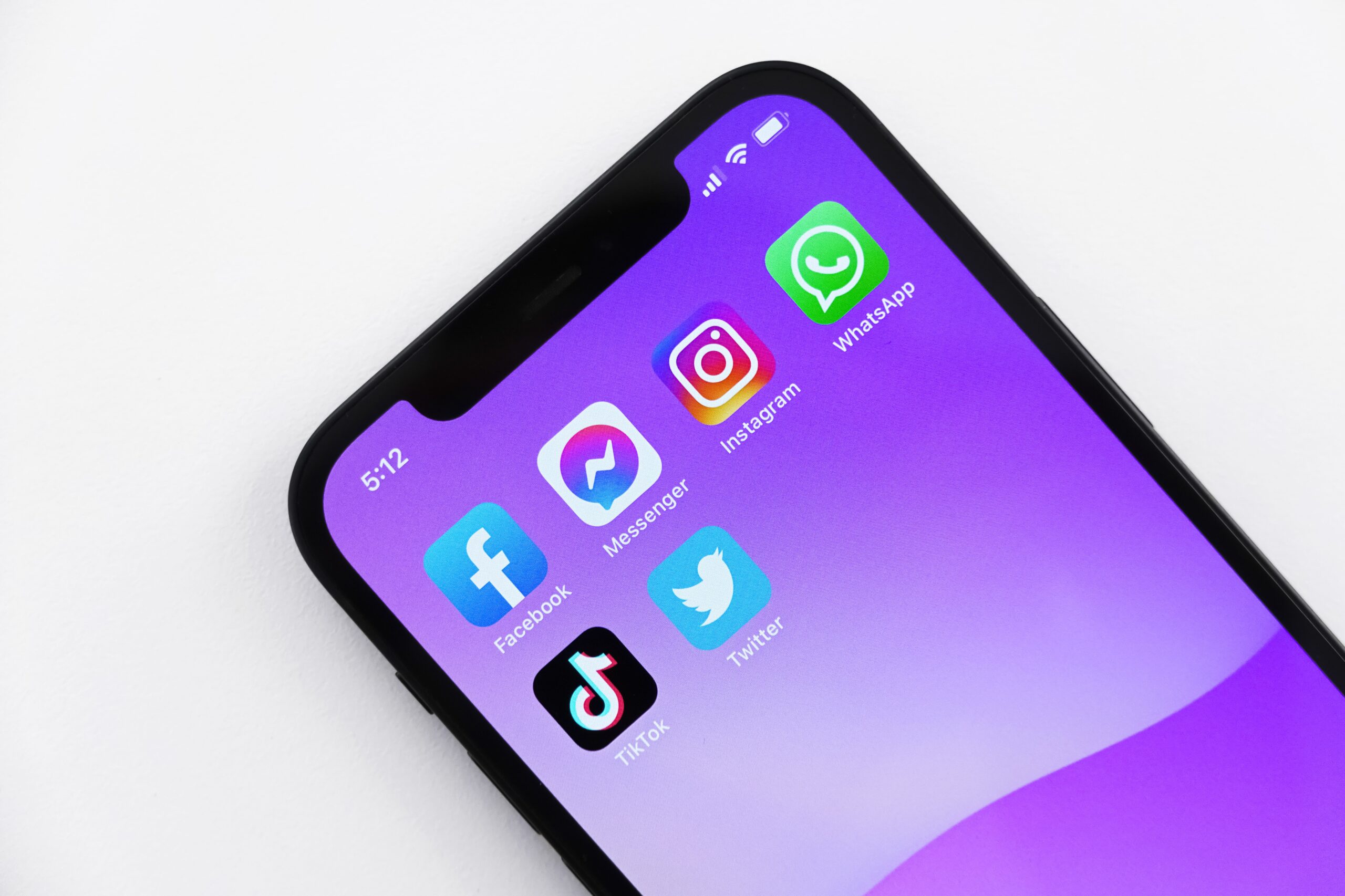 Close-up of a smartphone screen displaying icons of social media platforms including Facebook, Messenger, Instagram, Twitter, TikTok, and WhatsApp on a purple background.