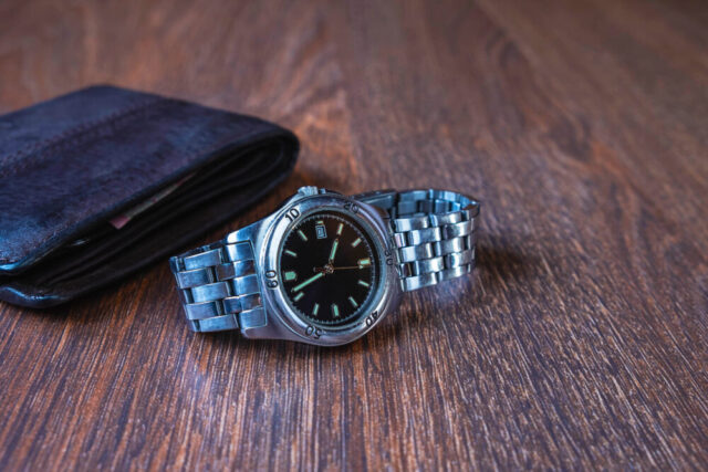 A stainless steel wristwatch and a folded leather wallet, both personal items, rest on a wooden surface.
