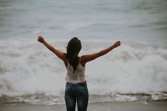 woman facing ocean with arms out