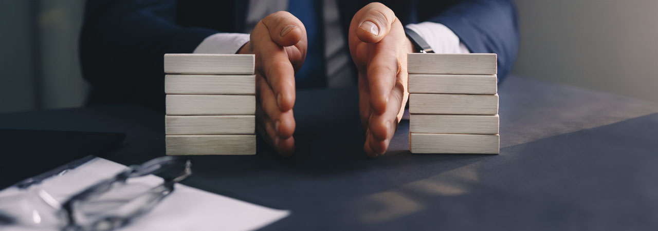 A professional in a suit sitting at a desk, arranging blank wooden blocks into two stacks, possibly simulating a planning or strategy concept.