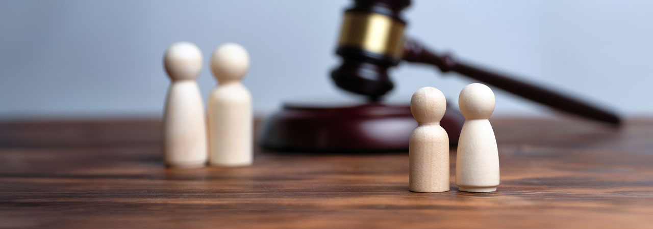 Two wooden figurines facing a judge's gavel on a desk, symbolizing a legal proceeding or judgment scenario.