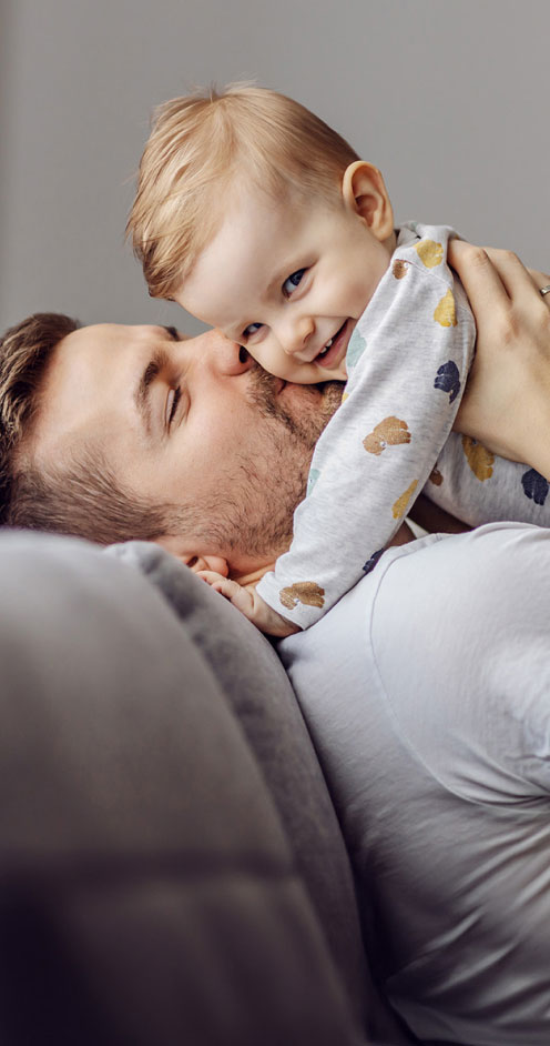 A playful interaction between a father and his young child unfolds in New Jersey. The father gently kisses the child's cheek as the child, wearing a bib with animal prints, giggles and hugs the father